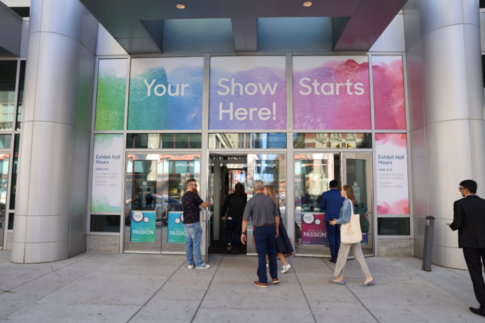 Several people walk through three sets of double doors to enter the Philly Convention Center, and signs above the doors read "your show starts here!"